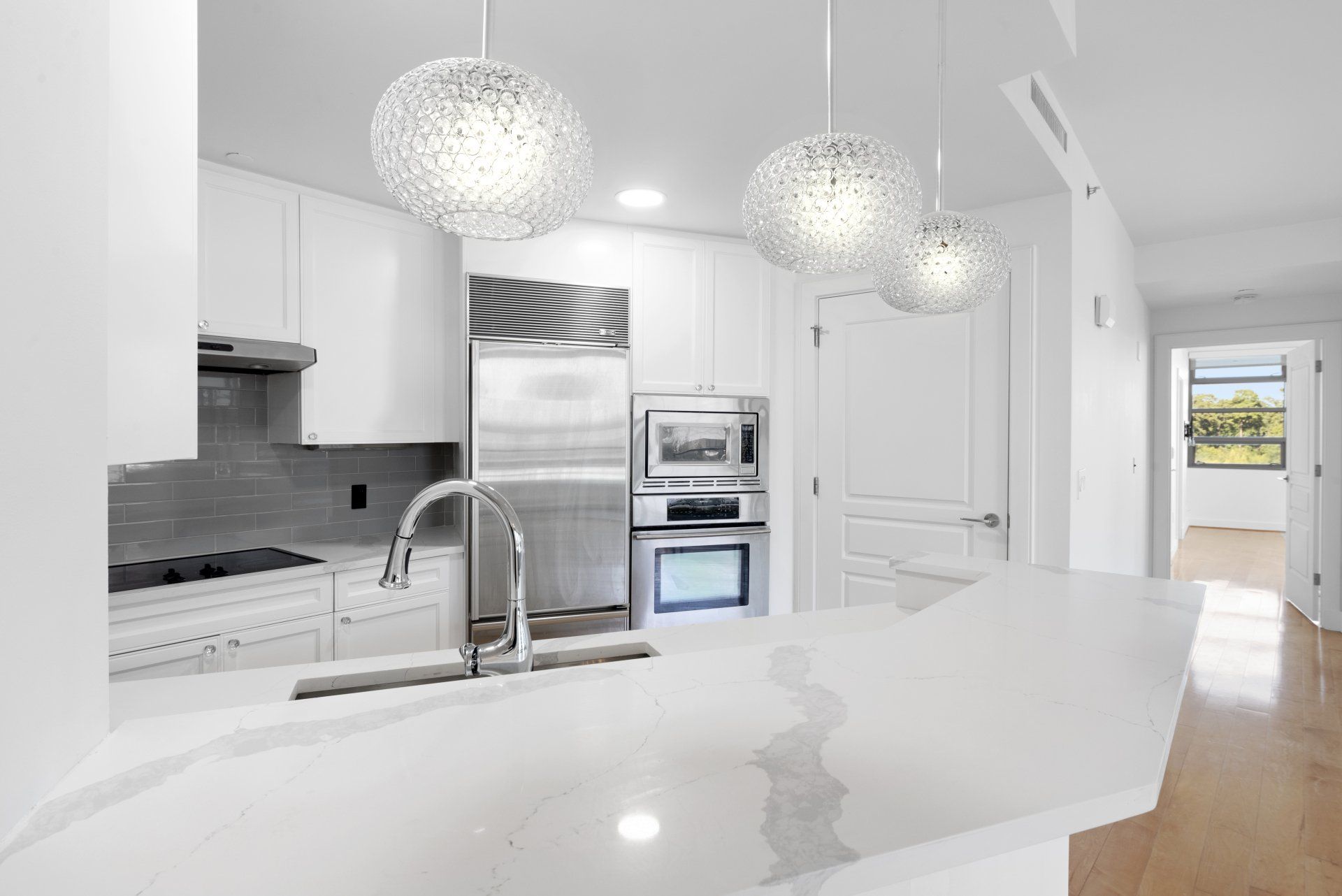 Modern white kitchen with stainless steel appliances, pendant lights, and quartz countertops.