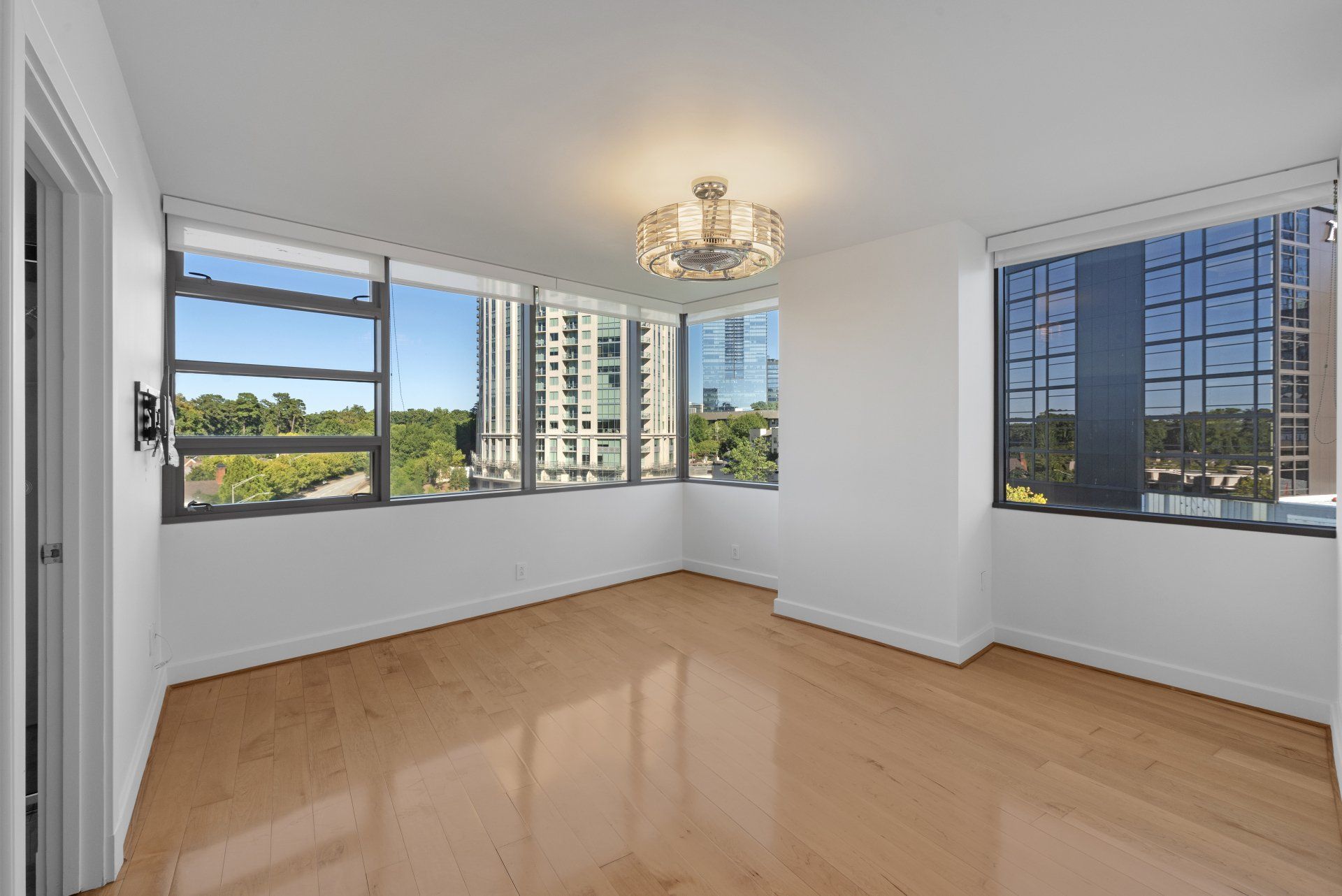 Empty room with hardwood floors, large windows, and a chandelier.