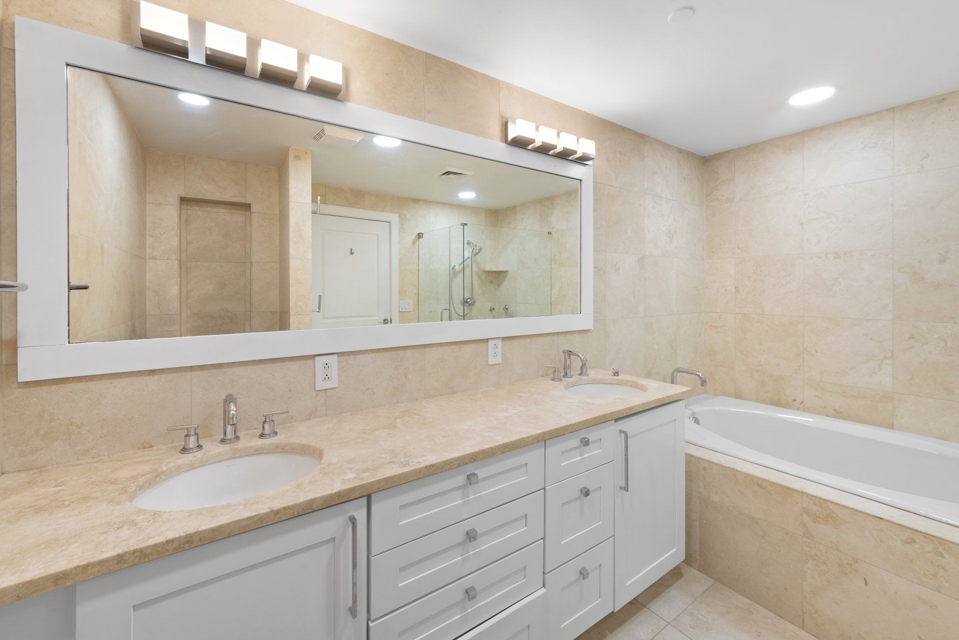 Bathroom with white vanity, large mirror, and beige tile.
