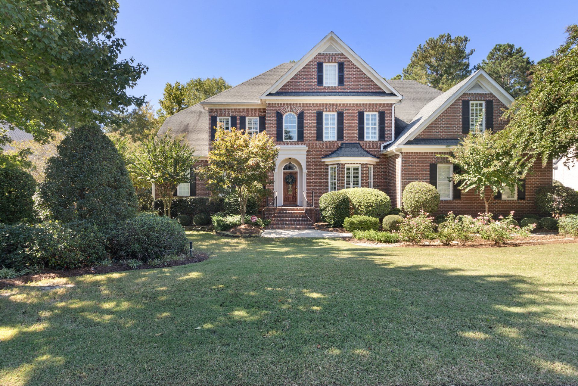 Two-story brick house with manicured lawn and landscaping on a sunny day.