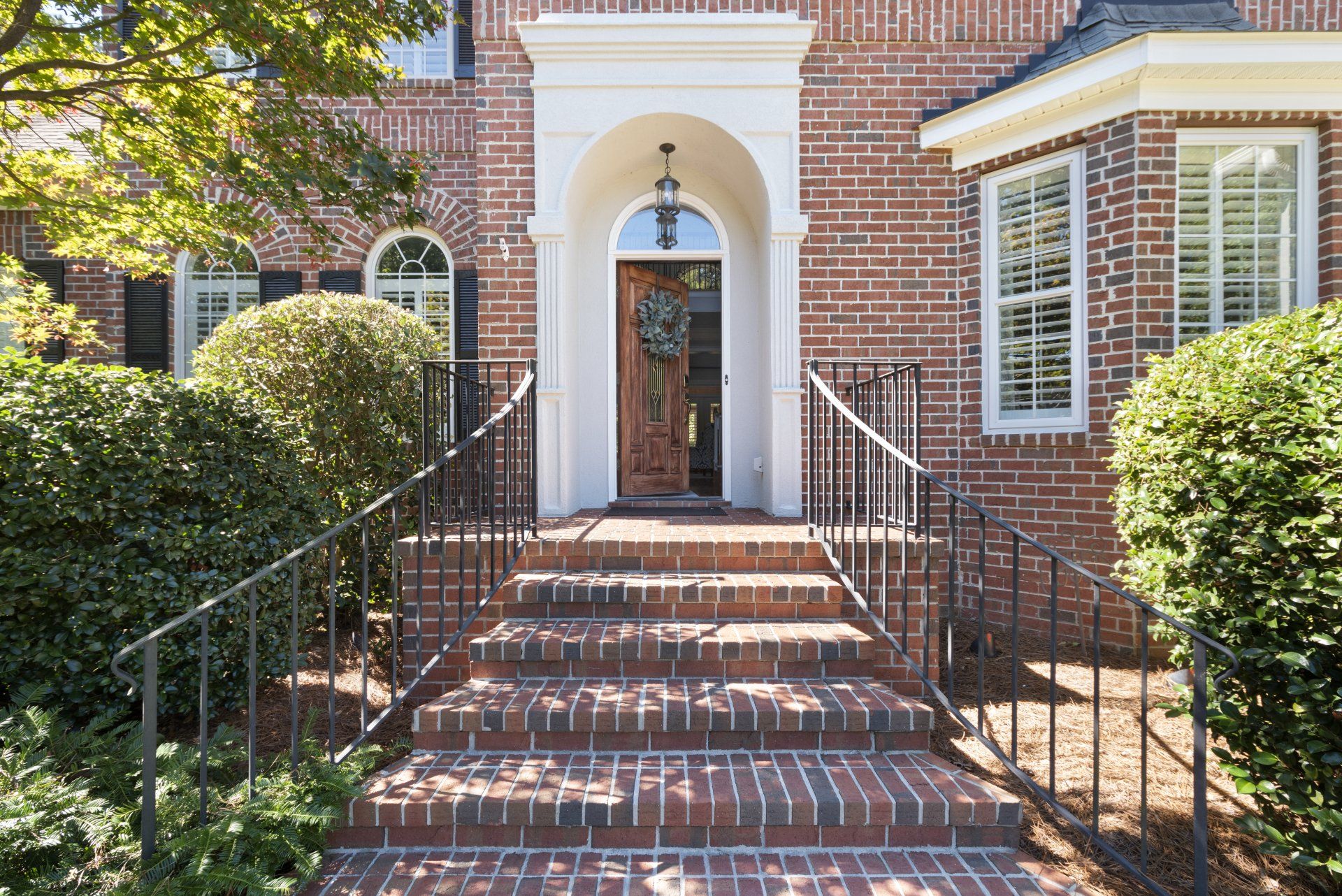 Brick house exterior with arched doorway, steps, and wrought iron railing.