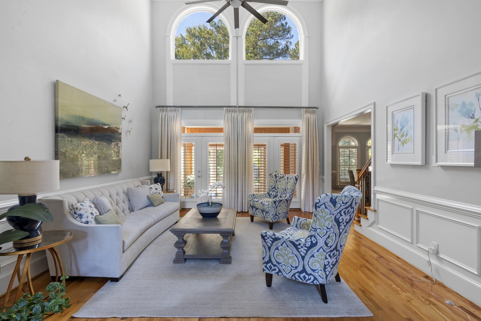Living room with high ceilings, arched windows, and light-colored furniture.
