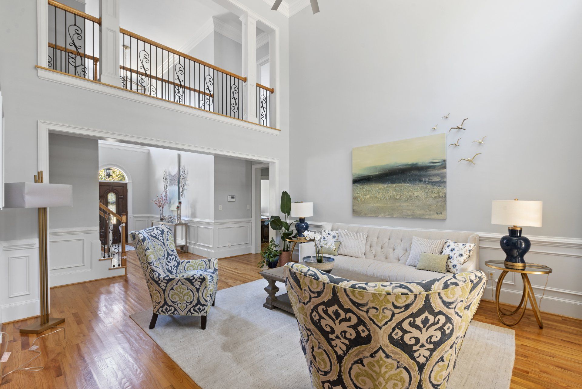 Spacious living room with high ceilings, hardwood floors, light gray walls, and ornate balcony.