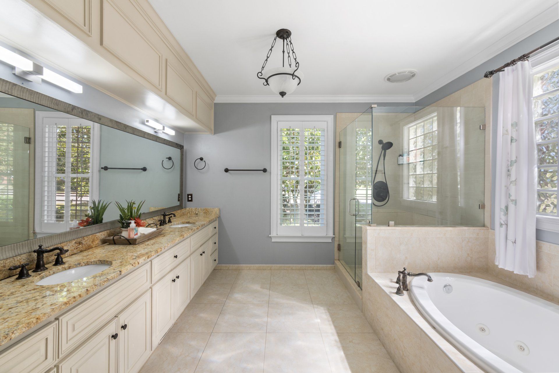 Spacious bathroom with beige cabinetry, granite countertops, large mirrors, a shower, and a jacuzzi tub.