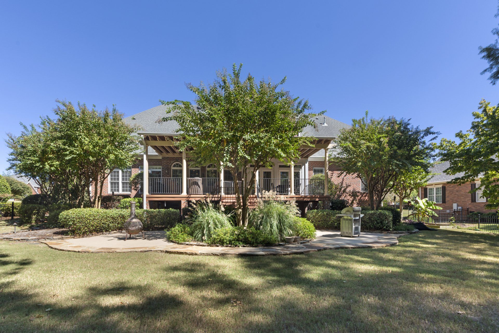 Backyard view of a house with a deck, trees, lawn, and a clear blue sky.