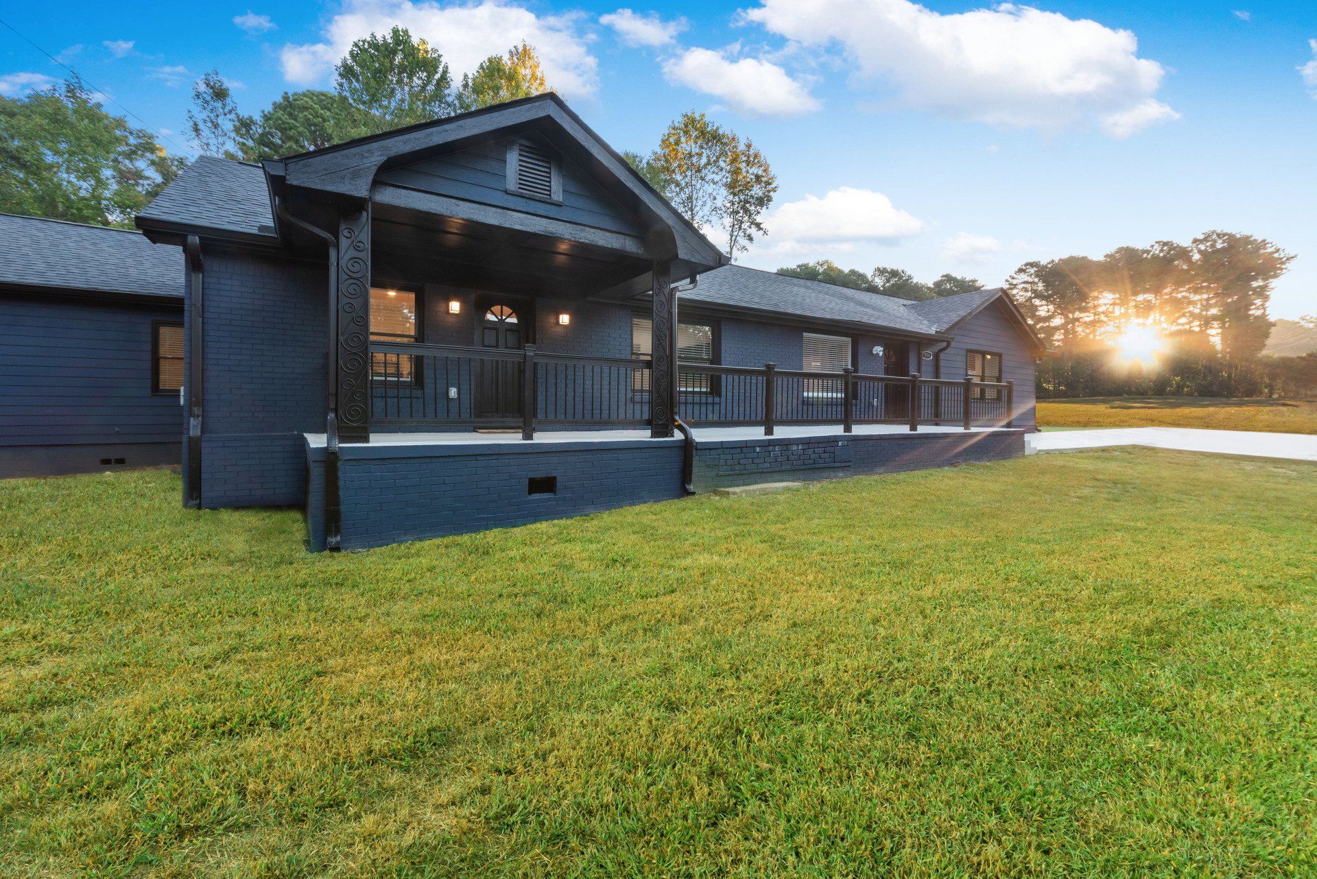 Dark blue house with black trim and a porch, set in a grassy yard under a sunny sky.