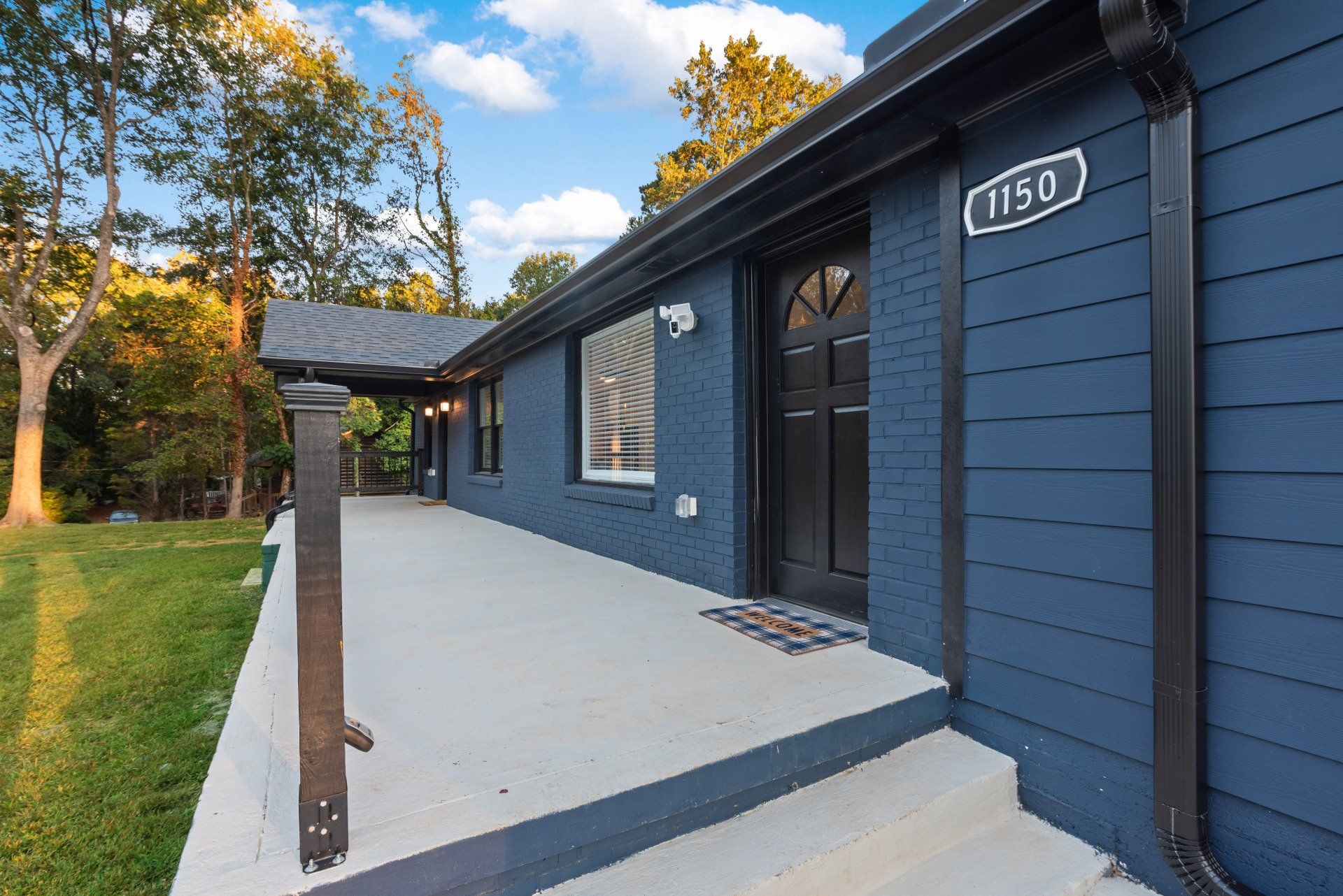 Blue house exterior with porch, steps, black door, and the address 