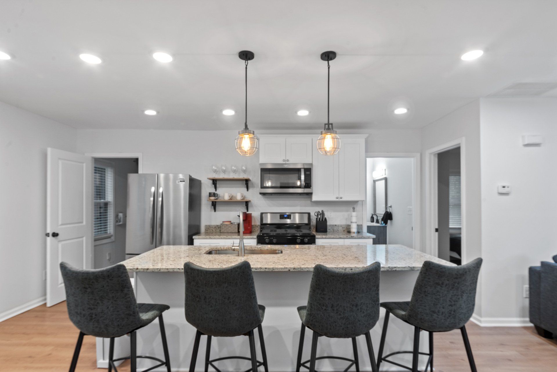 Modern kitchen with island, four bar stools, stainless steel appliances, and white cabinets.