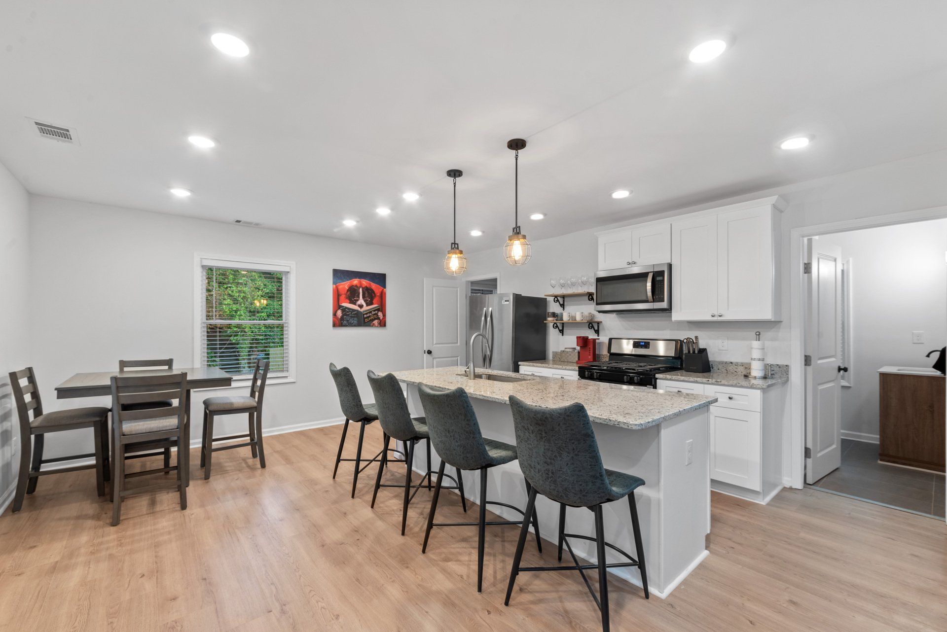 Modern kitchen with island seating, dining table, white cabinets, and stainless steel appliances.