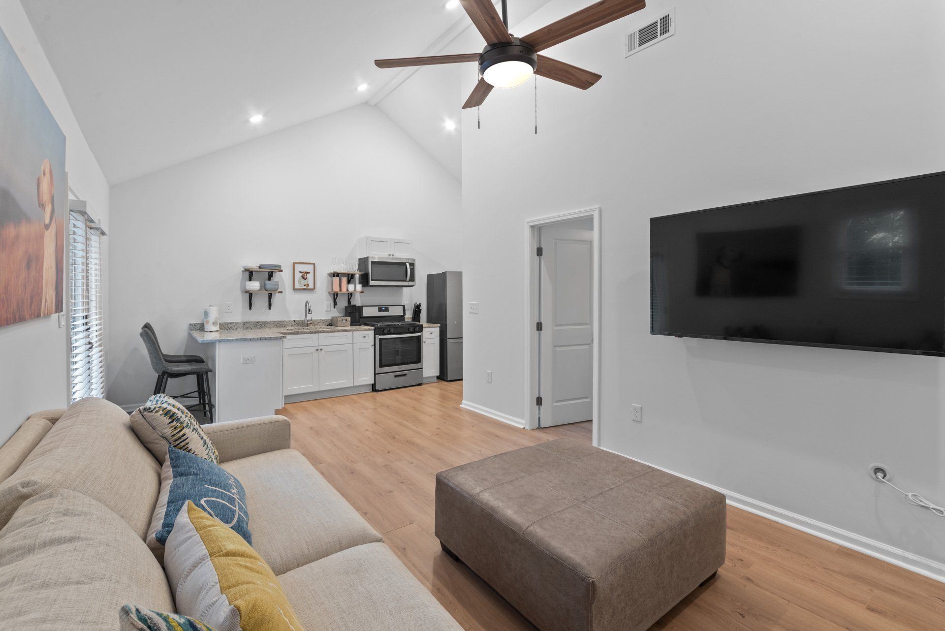 Modern living space with vaulted ceiling, kitchen, TV, sofa, and ottoman.