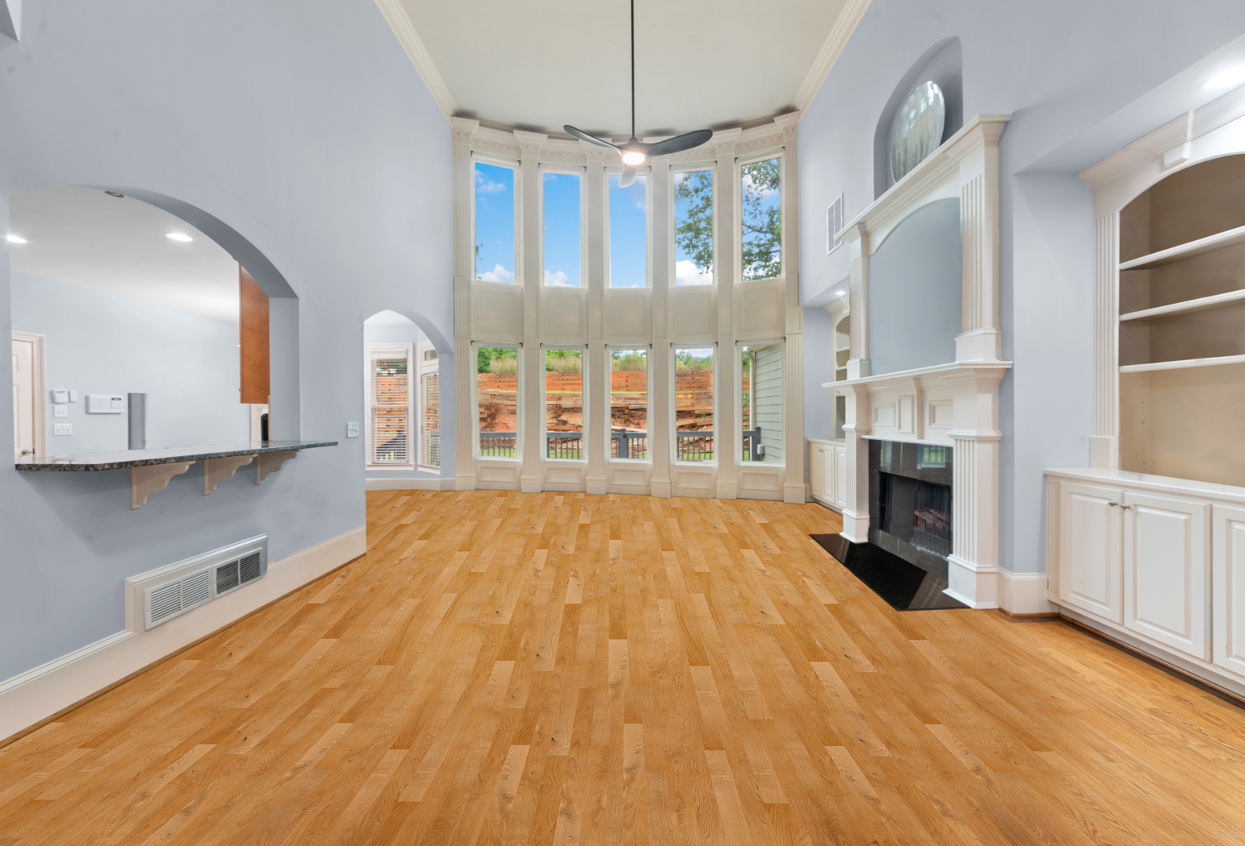 Image of an empty living room in a home. It features a fireplace and nice floor to ceiling windows.