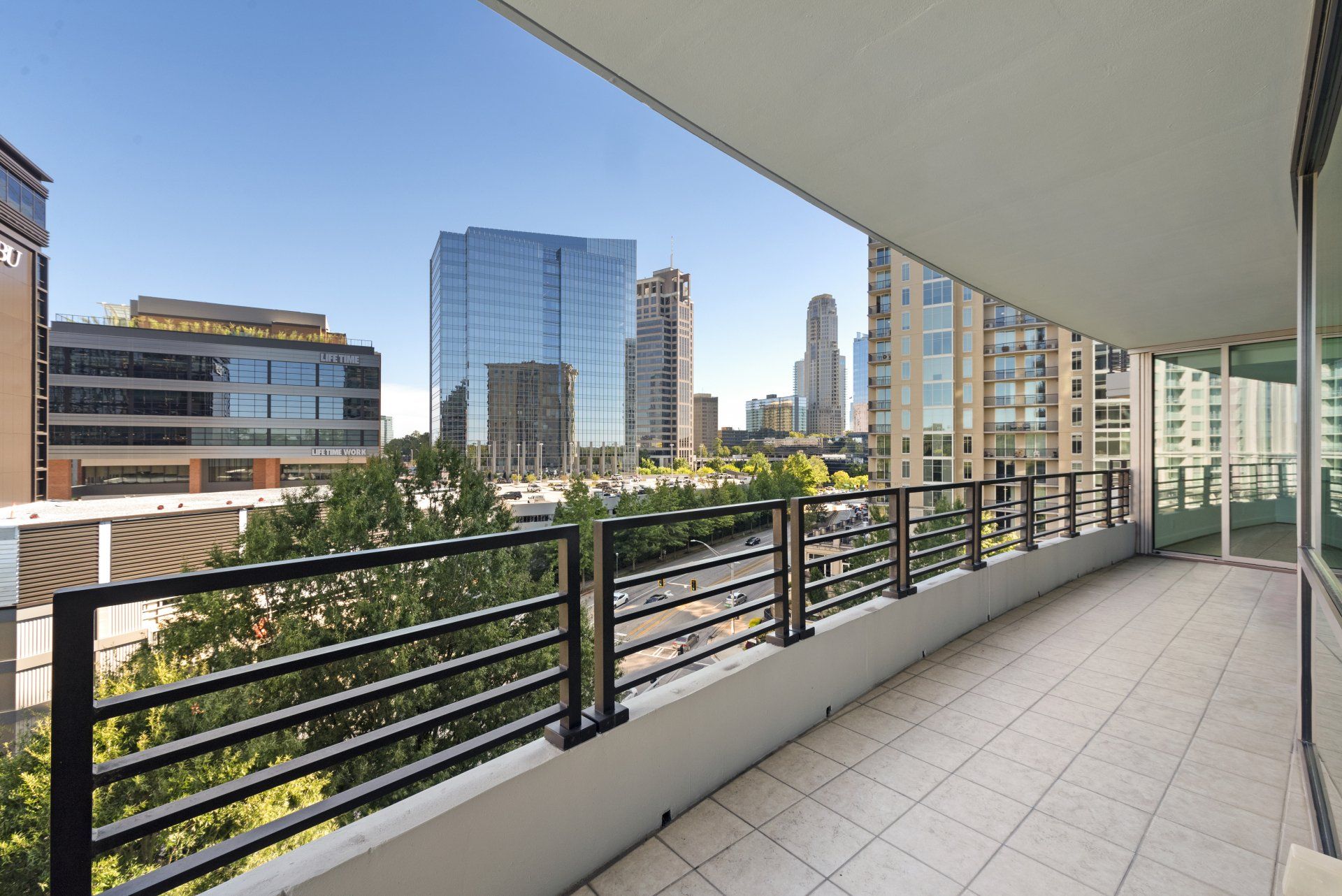 Balcony overlooking a city skyline with glass and metal railings. Sunny day, modern buildings in view.