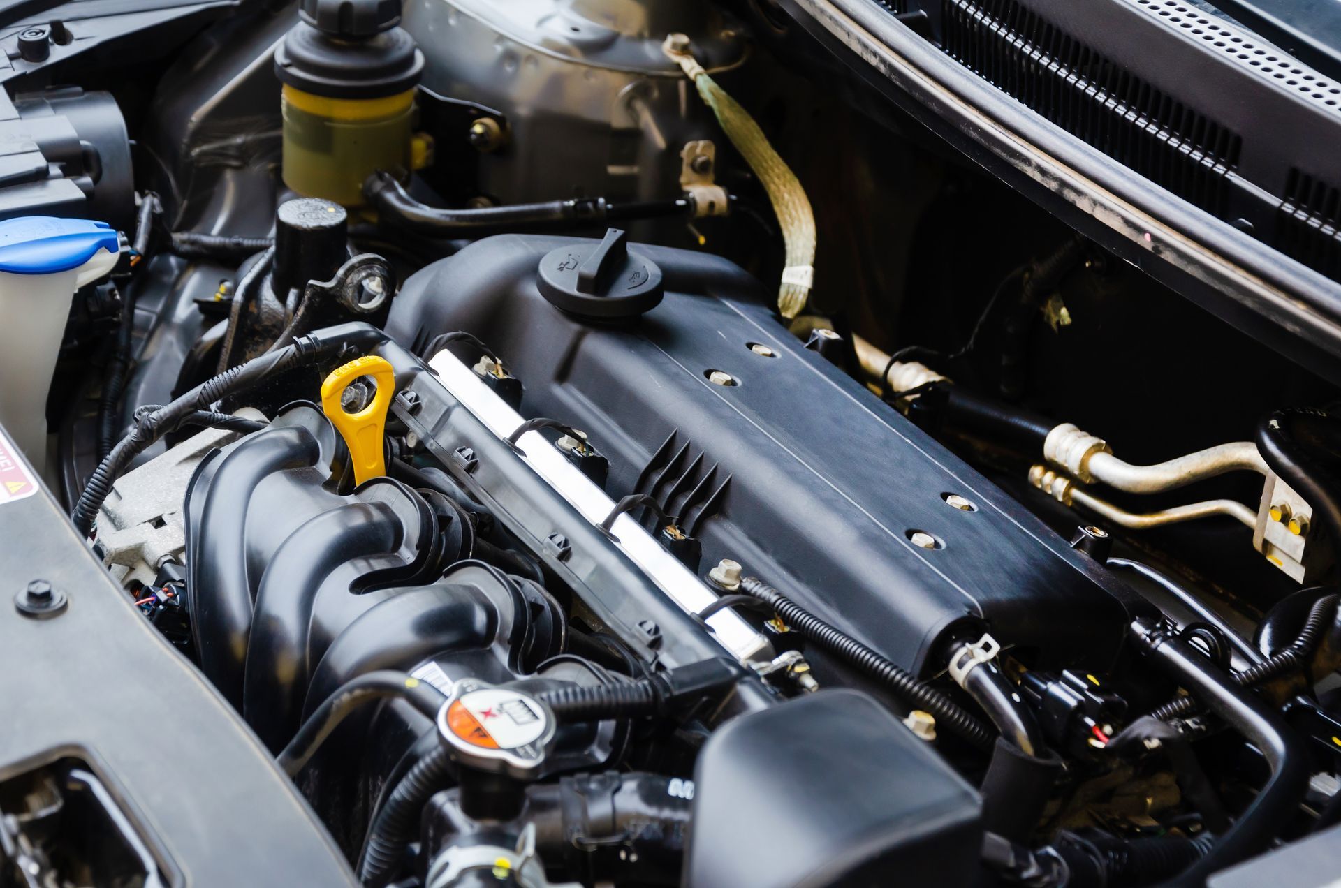 Car engine bay with black components and a yellow oil dipstick under the hood