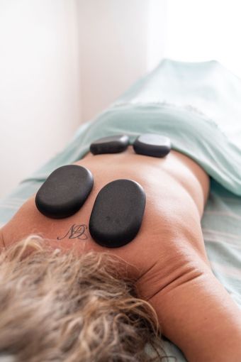 Een persoon krijgt een hot stone massage op de rug, waarbij de stenen langs de wervelkolom worden geplaatst.