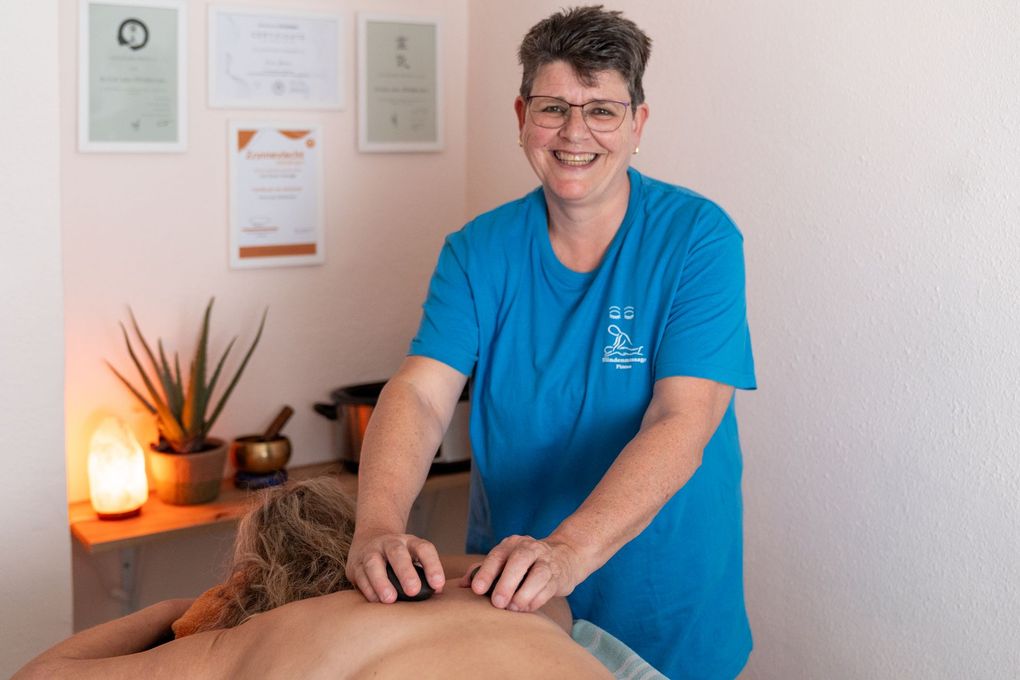 Vrouw geeft een andere persoon een hot stone massage, binnen.