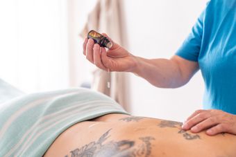 Iemand die een klein, donker flesje boven iemands rug houdt; massage of behandeling is gaande.