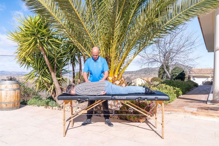 Een massagetherapeut geeft een rugmassage in de buitenlucht, onder een palmboom.