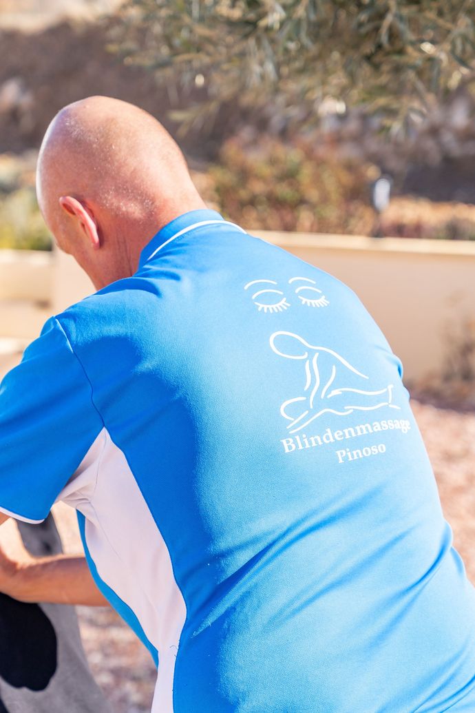 Man in blauw shirt met massagelogo, buiten.