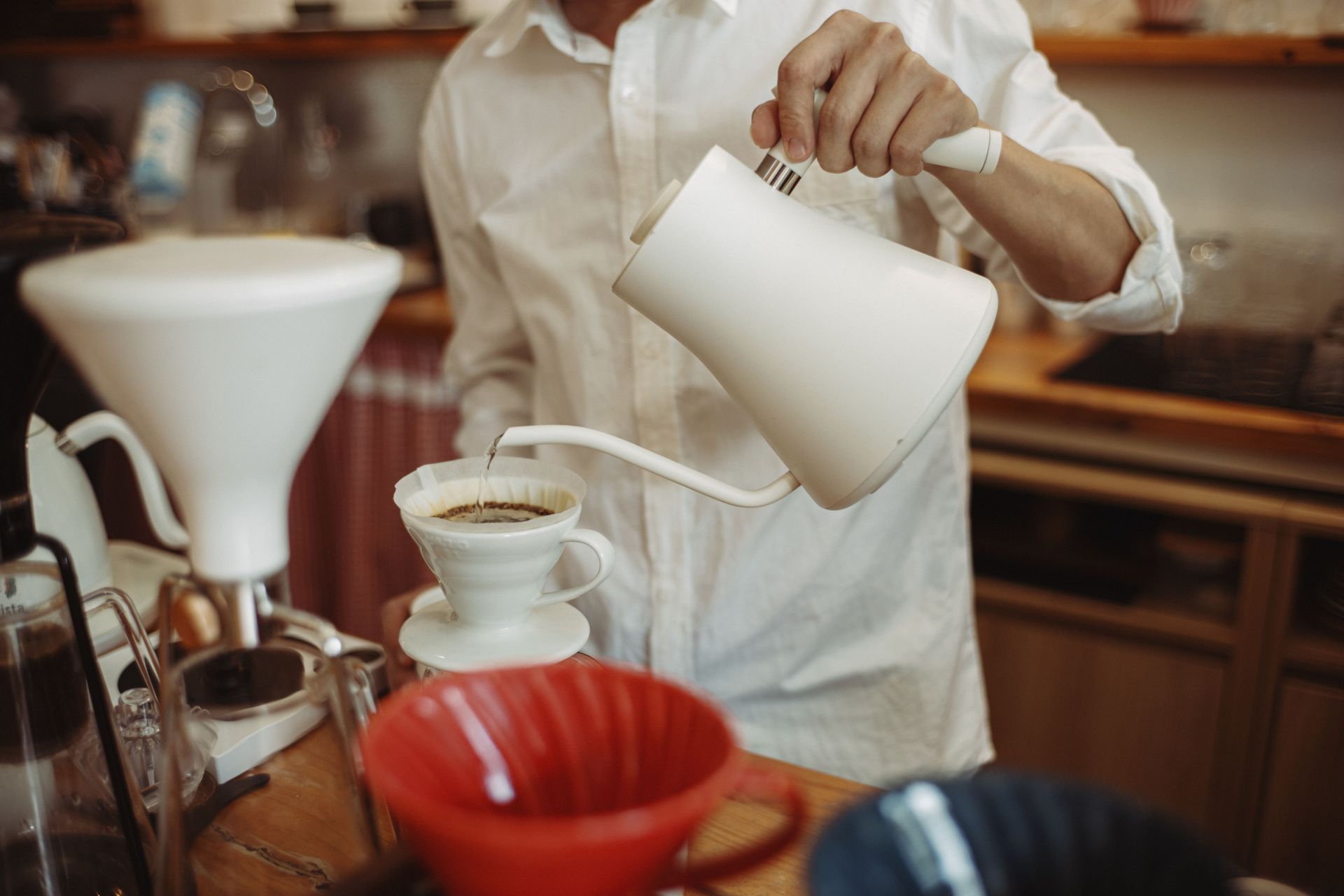 Barista pouring hot water into a coffee filter in a café, with cups and brewing tools on the counter
