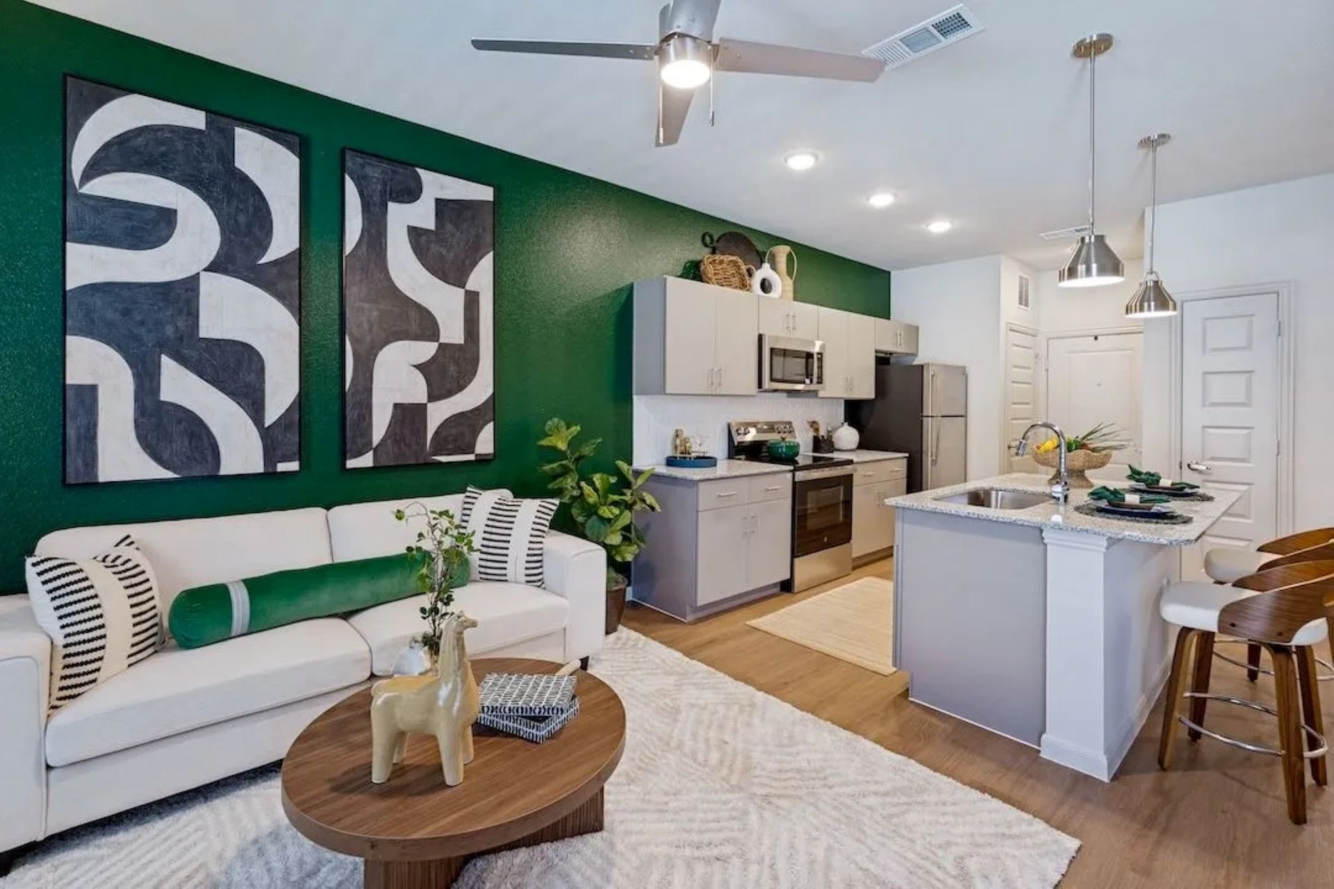 An open-concept apartment interior featuring a green accent wall, white sofa, abstract art, and kitchen island.