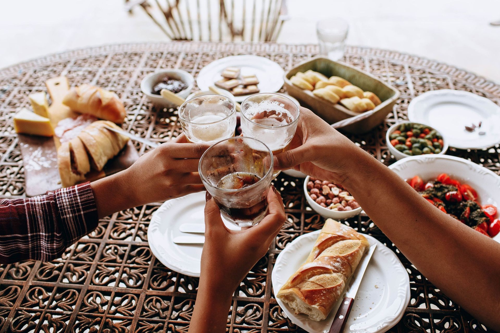 Three people holding glasses and toasting while sitting around a patterned table filled with bread and fresh food.