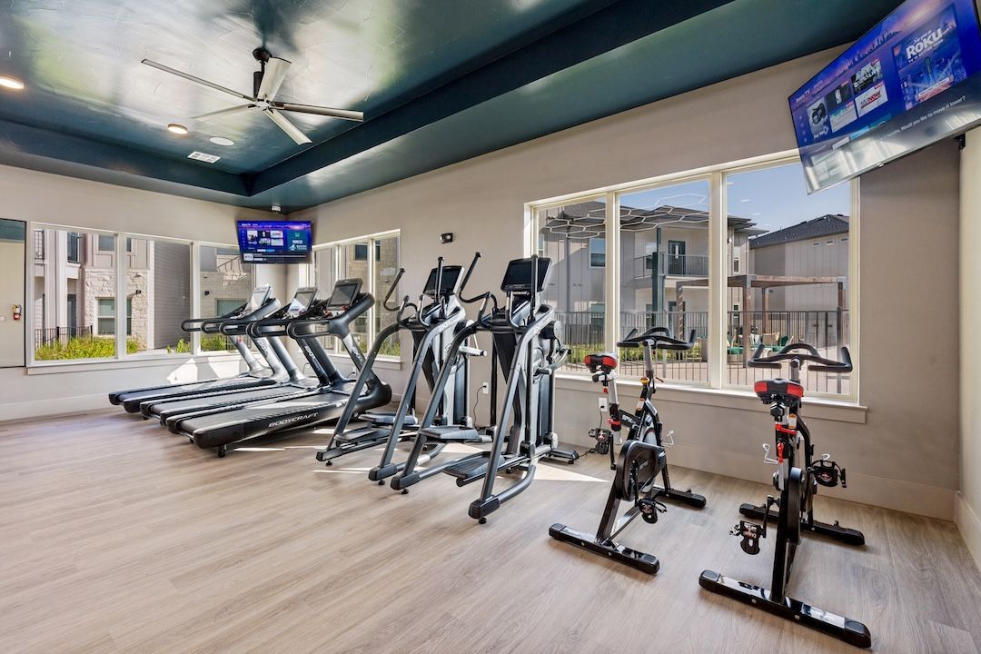 Modern gym with treadmills, ellipticals, and spin bikes in a bright room with large windows.
