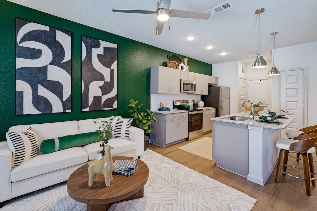 Bright living room with green accent wall, white sofa, kitchen island, and abstract wall art