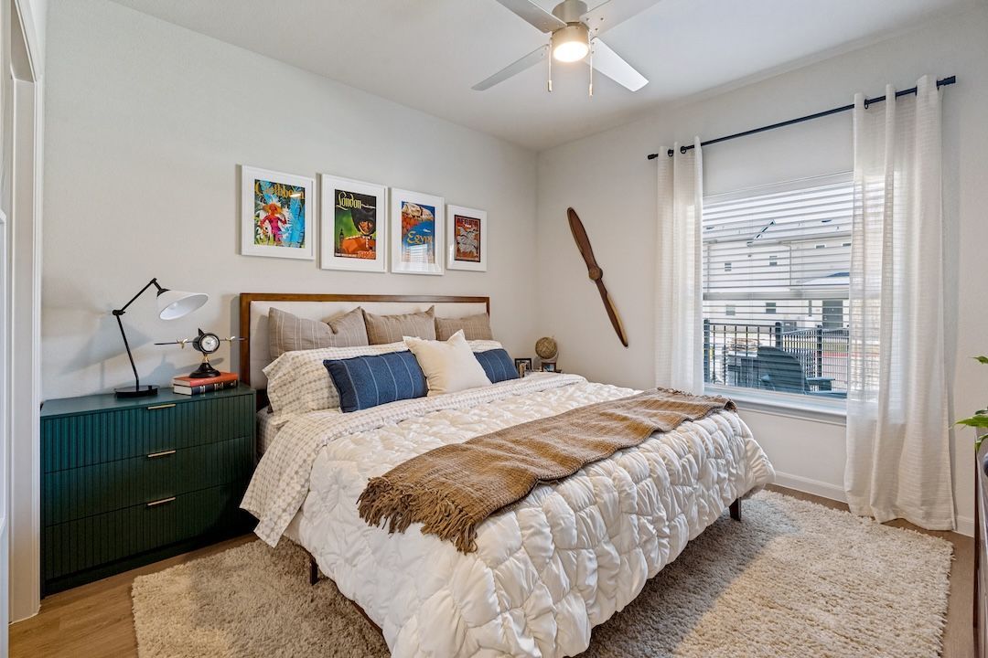 Bright bedroom with a queen bed, teal nightstand, wall art, and a window with white curtains.