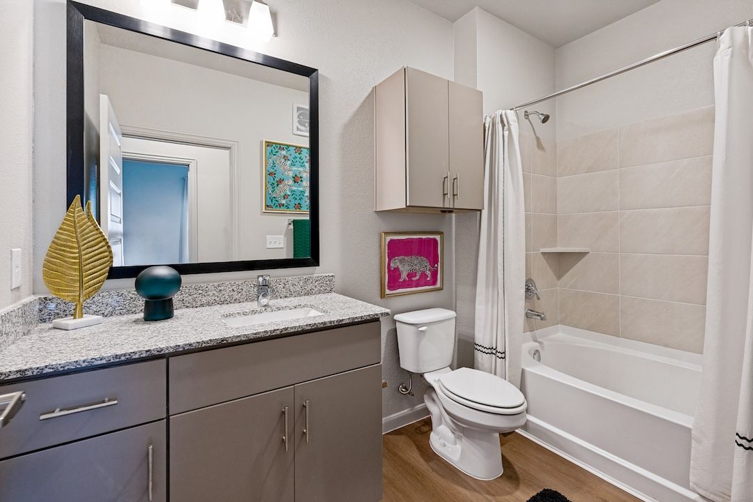Modern bathroom with gray vanity, mirror, toilet, tub, and beige tile accents