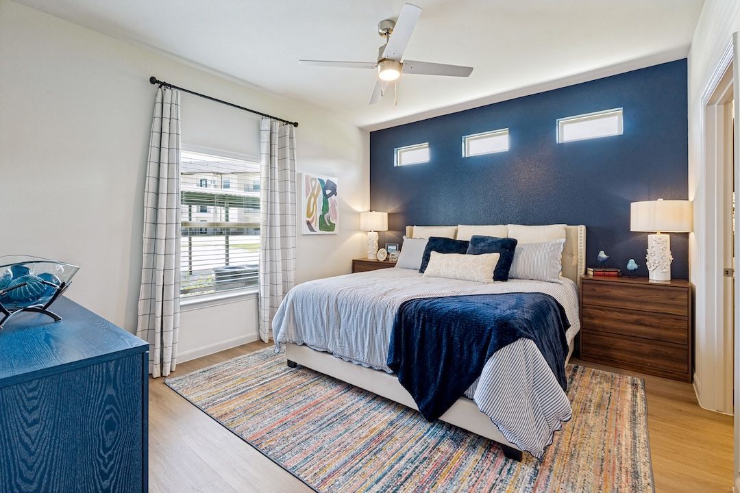 Bright bedroom with blue accent wall, king bed, nightstands, and a striped rug by a glass door.