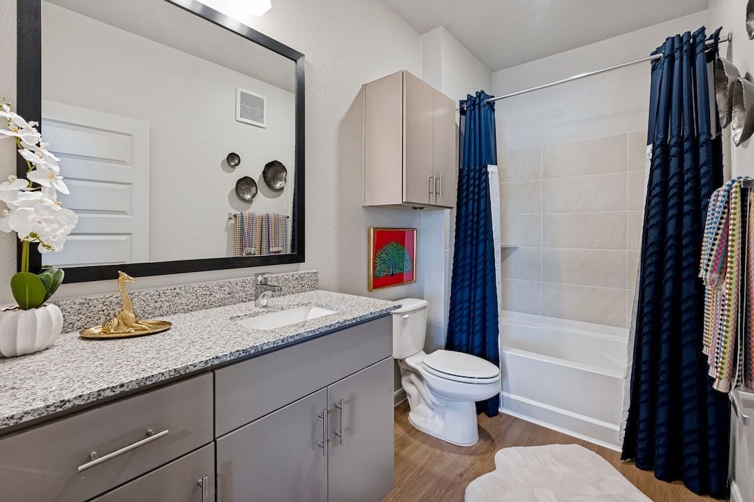 Modern bathroom with gray vanity, large mirror, shower curtain, and beige tile floor