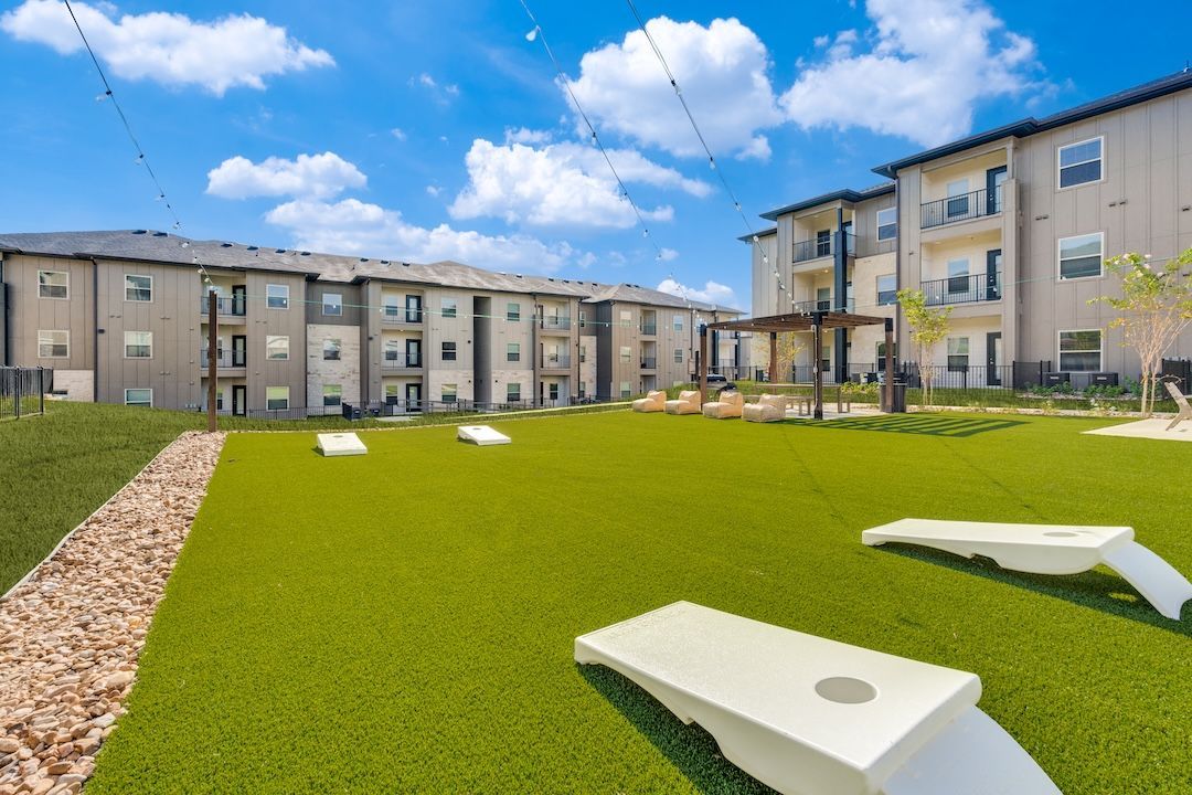 Modern apartment courtyard with green turf and white cornhole boards under a blue sky