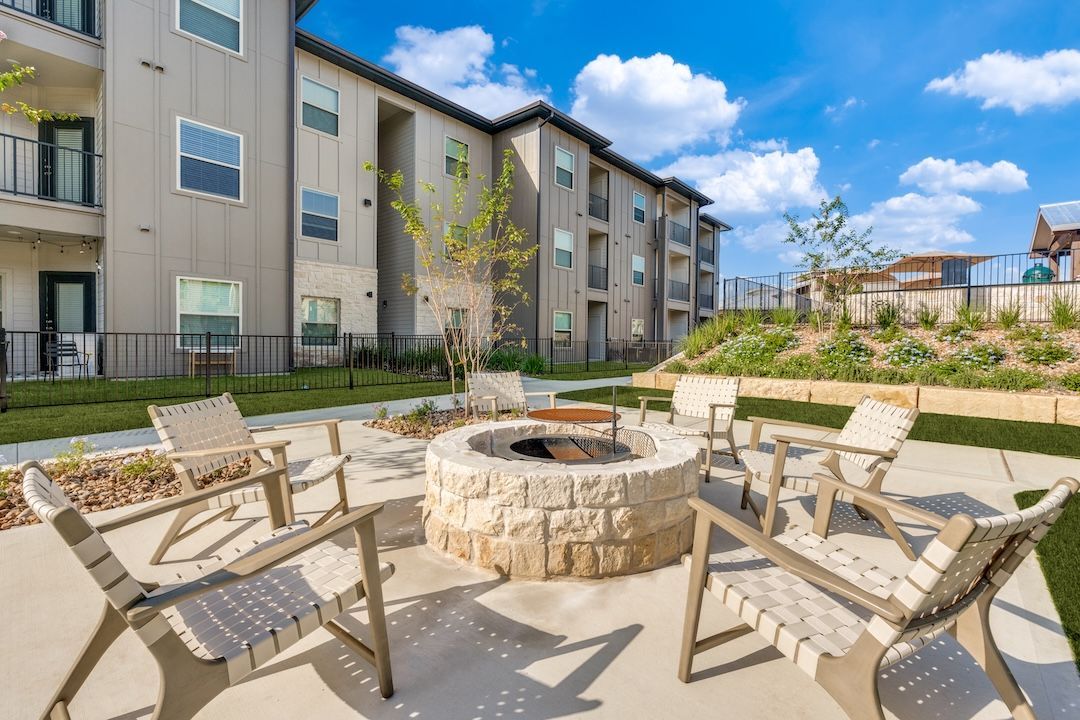Apartment courtyard with stone fire pit, tan lounge chairs, and modern buildings under a blue sky
