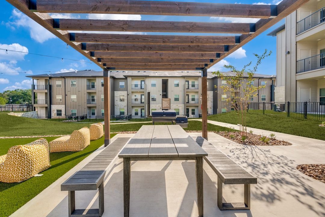 Outdoor picnic area with pergola, picnic tables, and apartment buildings in the background