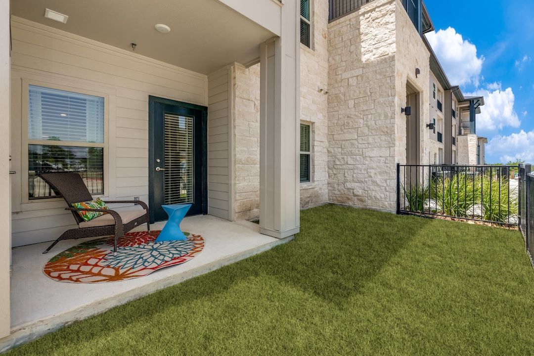 Patio with chairs and colorful rug beside a grassy yard outside a modern home