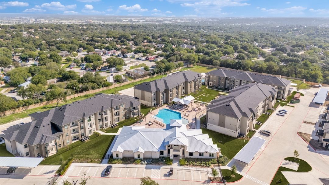 Aerial view of a large apartment complex with a central pool and surrounding neighborhood
