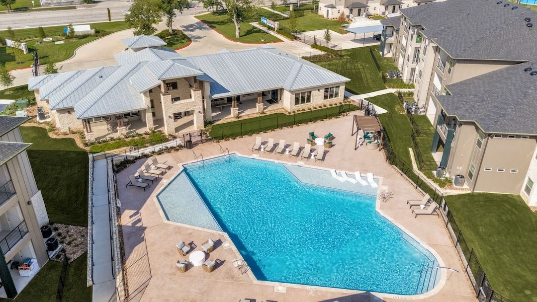 Aerial view of an apartment pool area with a bright blue swimming pool and lounge chairs.