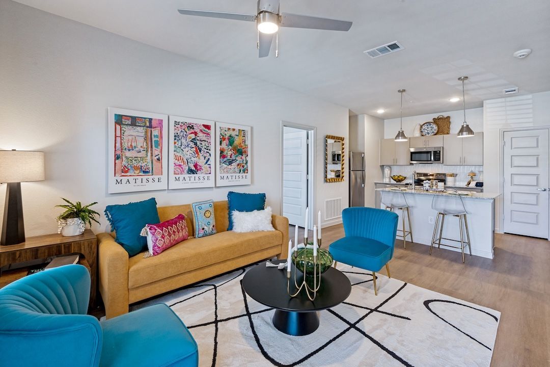 Bright modern living room with teal chairs, tan sofa, black coffee table, and open kitchen bar stools