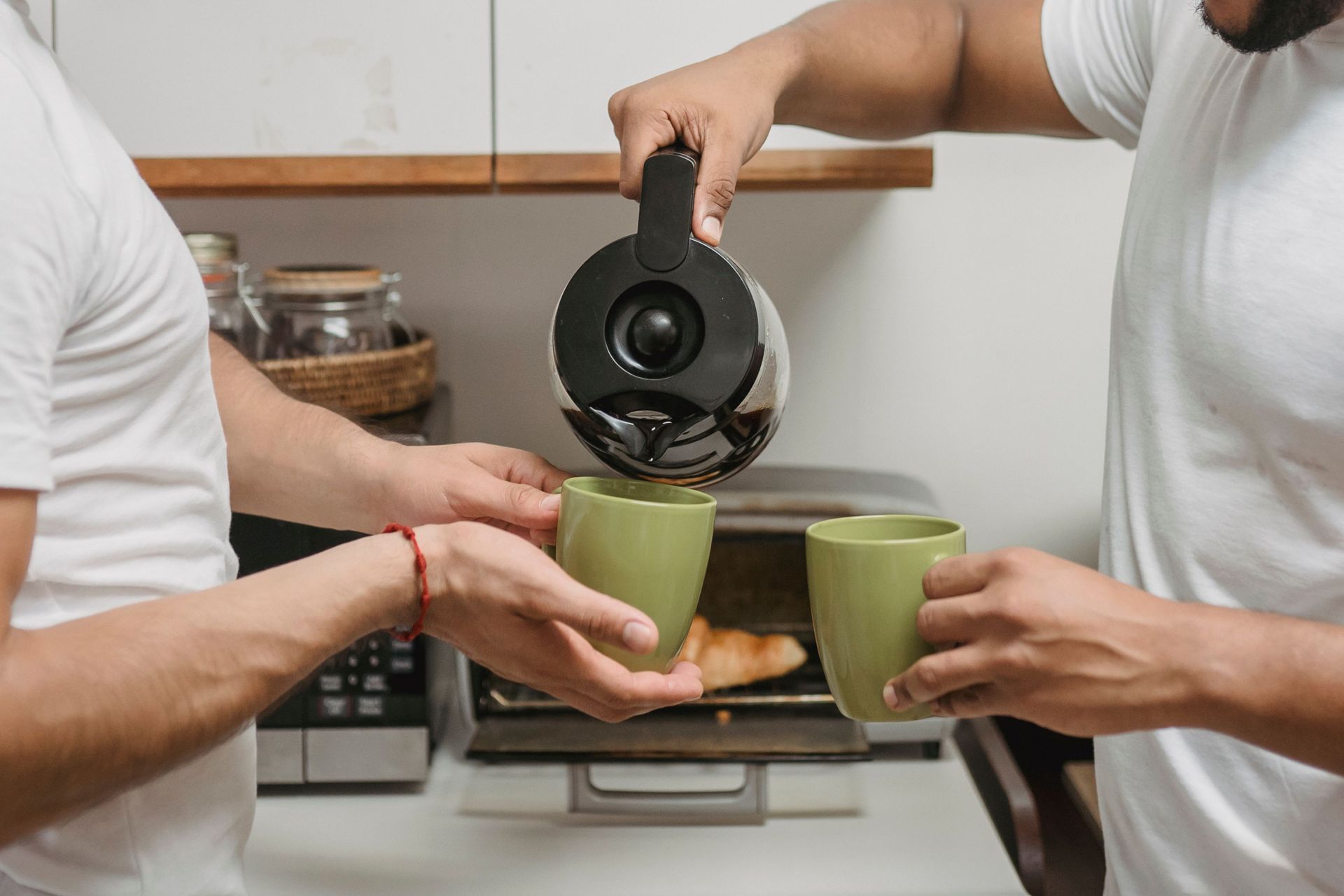 Two people wearing white shirts standing together with one pouring coffee from a coffee pot into a green mug.