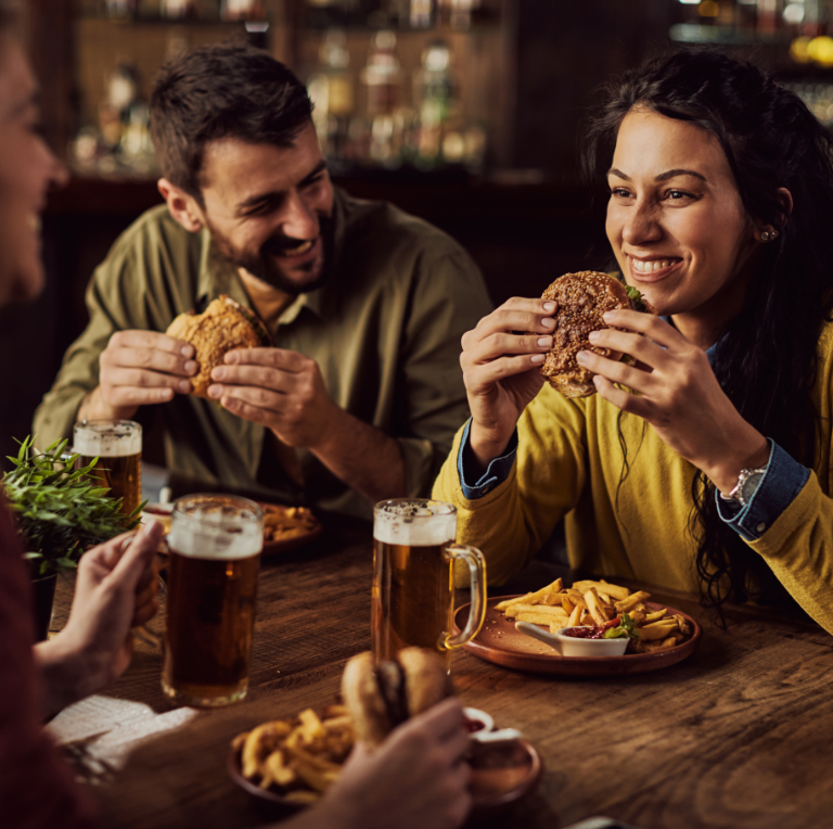 Friends sharing burgers and beer at a cozy bar table, smiling and chatting.