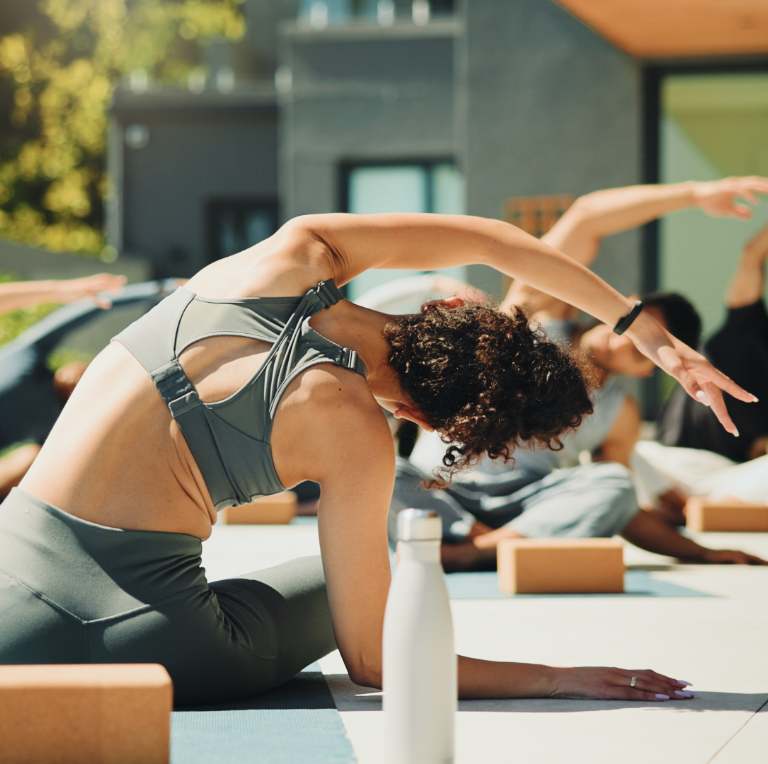 People doing yoga stretches outdoors on a sunny patio with mats and blocks.