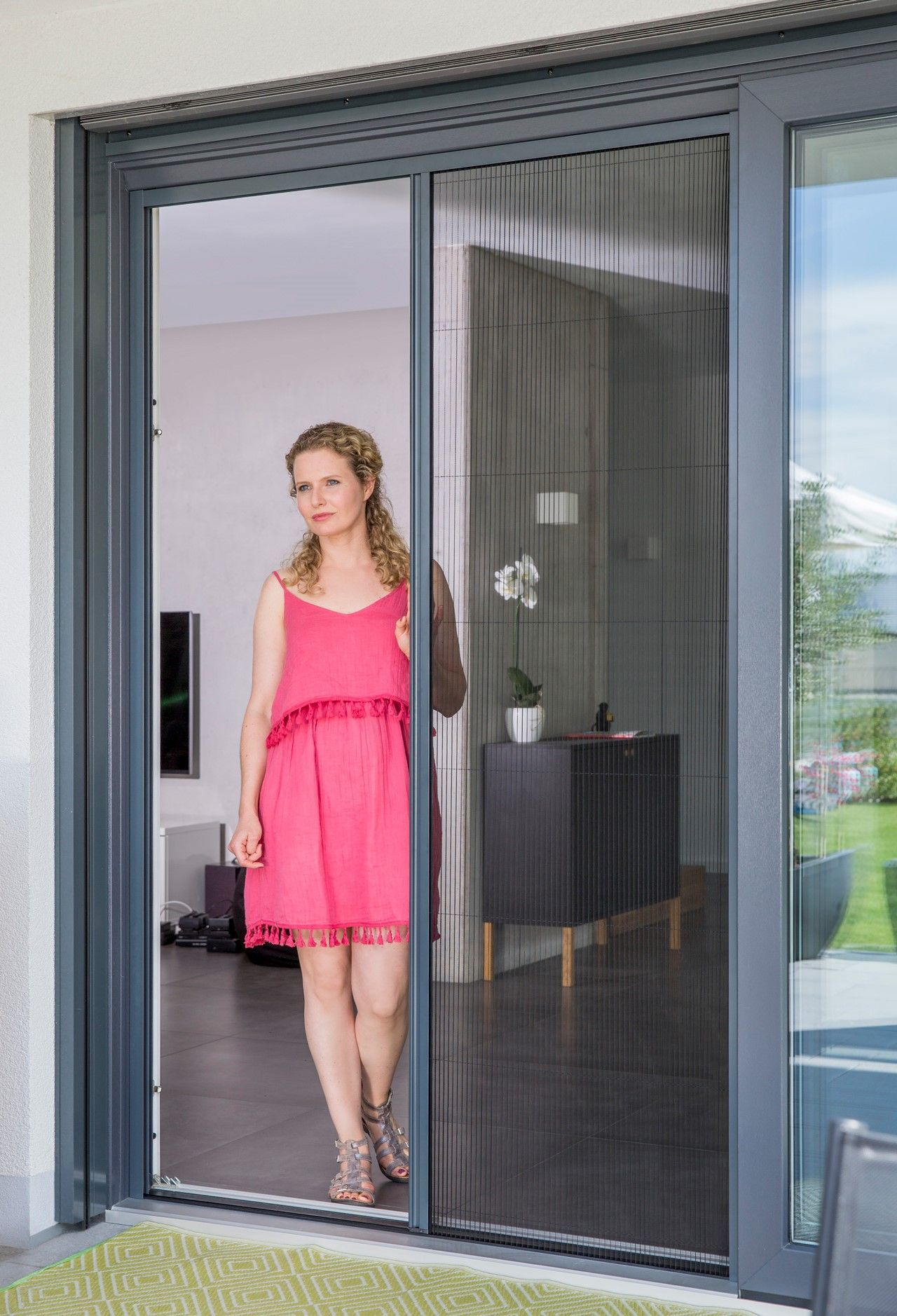 Femme en robe rose debout dans l'embrasure d'une porte moustiquaire.