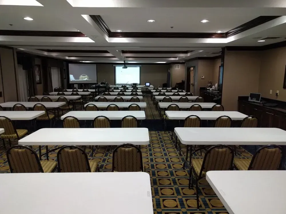 Empty conference room with rows of tables and chairs facing a projection screen and stage.