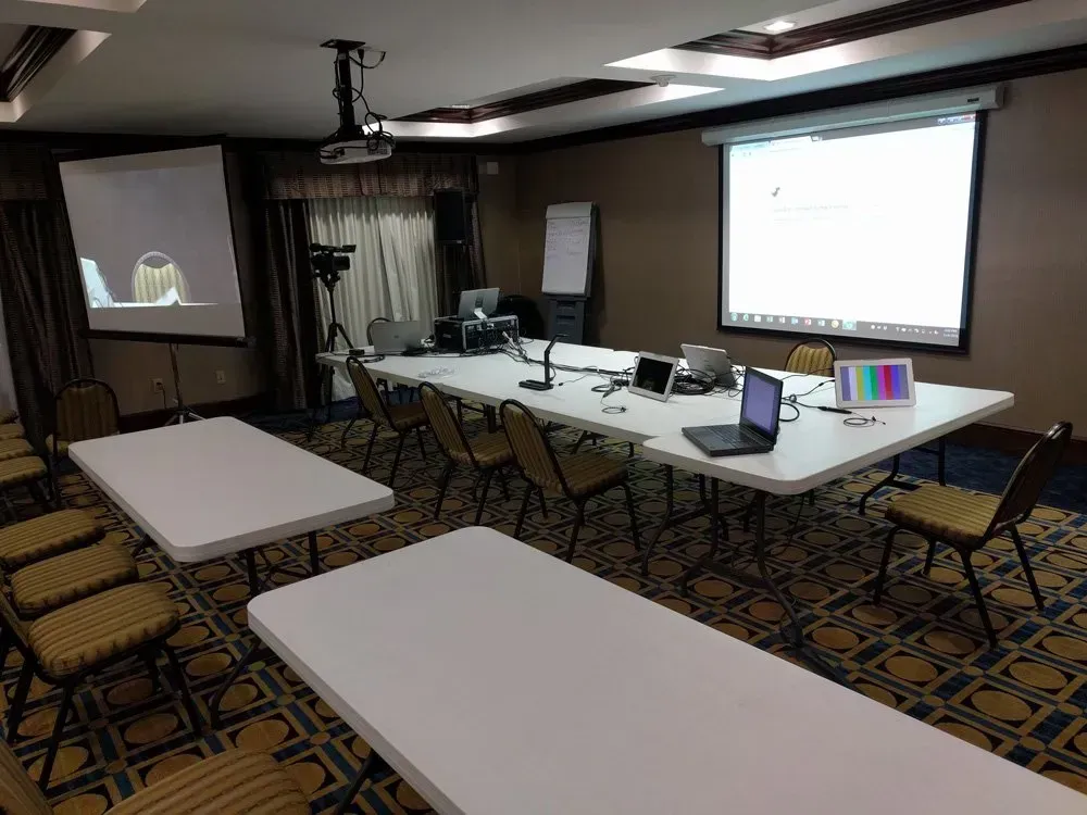 Conference room with projector screen, laptop, tables, and rows of folding chairs set up for a presentation