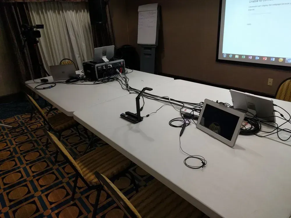 Conference room table with microphones, cables, and a projector screen at the front