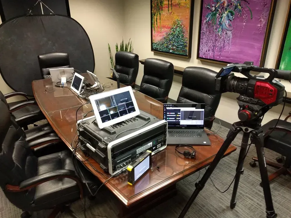 Podcast studio with laptops, microphones, mixer, and tripod in a conference room