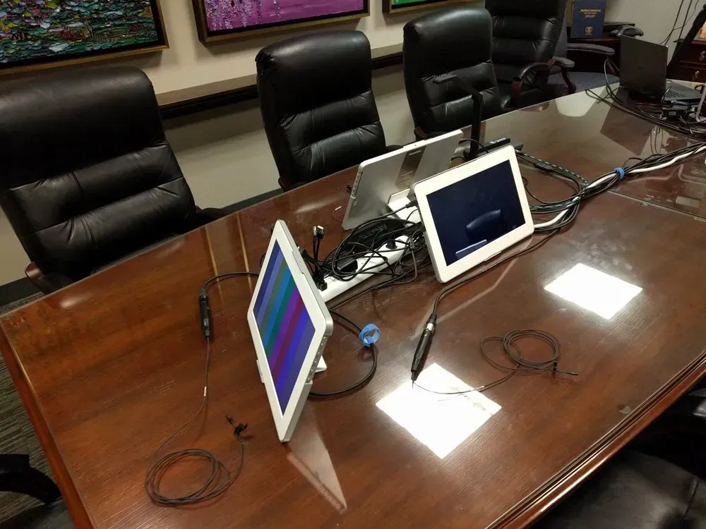 Conference room table with two tablets, cables, and microphones set up for a meeting
