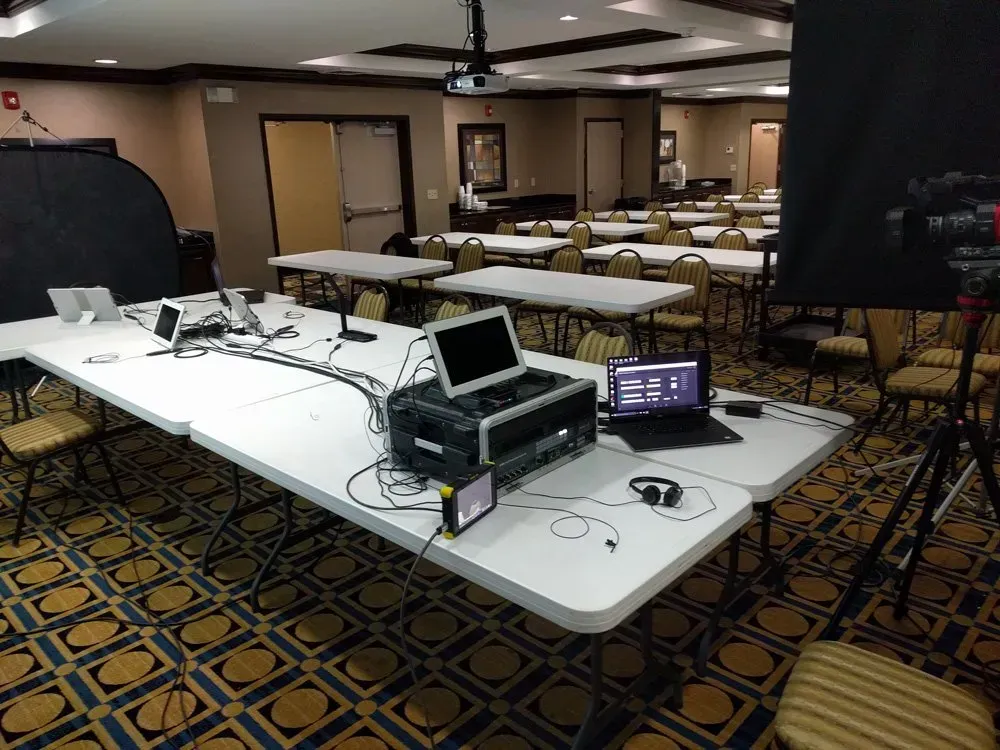 Conference room with tables, chairs, and audio-visual equipment set up at the front.