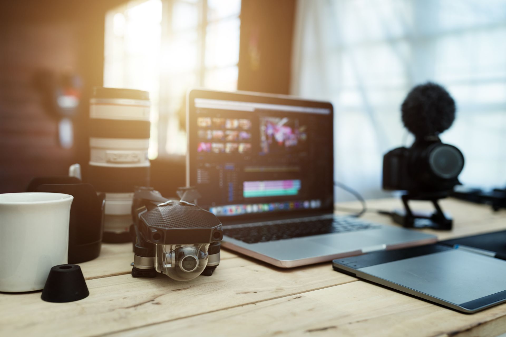 Workspace with laptop, camera, tablet, and coffee mug on a sunlit desk