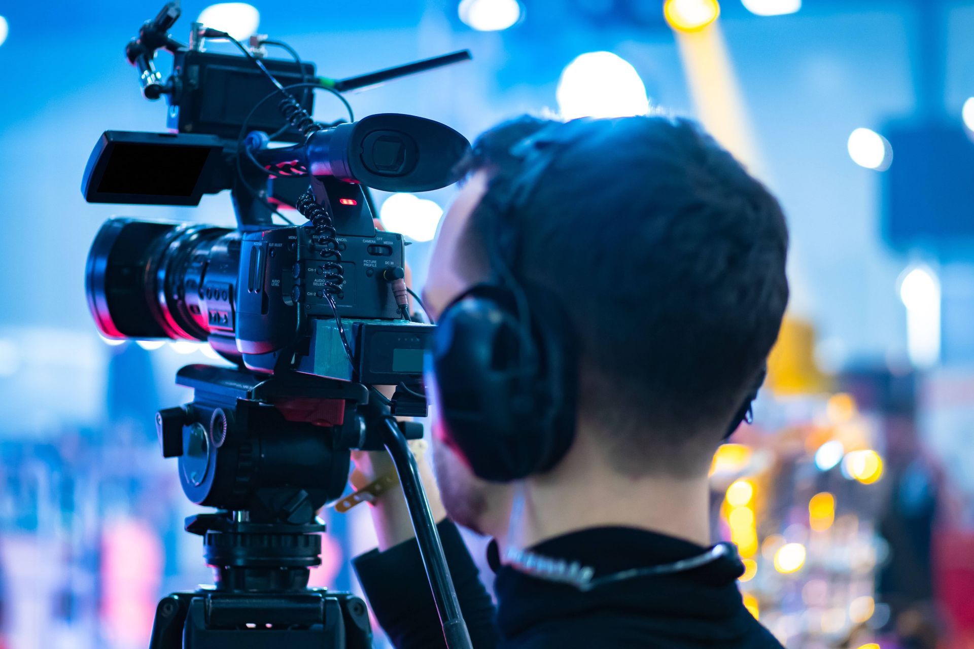 Videographer filming with a professional camera and headphones in a blurred blue-lit studio setting